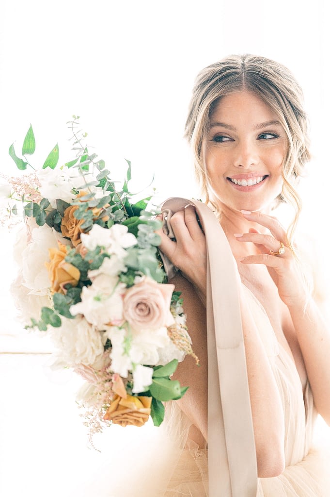Photo edited by Refined Preset KT Merry of a beautiful bride holding a bouquet and laughing towards the side of the camera.